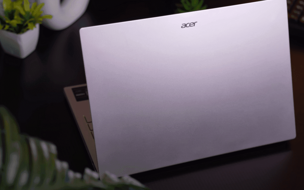 Top view of an Acer laptop with a silver finish, partially open on a dark desk surrounded by plants.