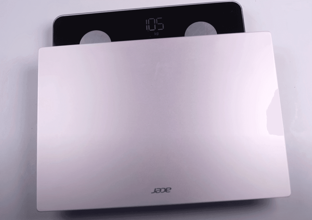 An Acer laptop is placed on a digital weighing scale showing a weight of 1.05 kilograms.
