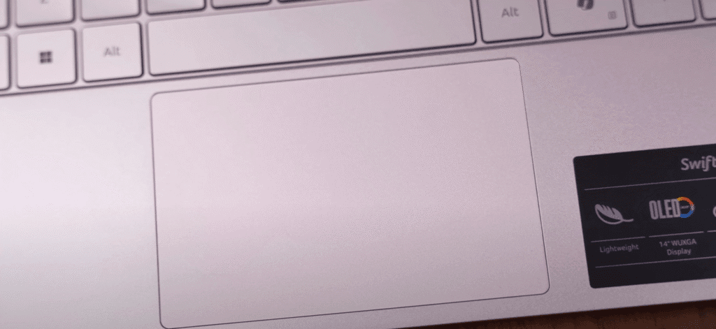 Close-up of Acer Swift laptop touchpad area showing a large smooth trackpad and an OLED display sticker highlighting lightweight design and 14-inch WUXGA screen.