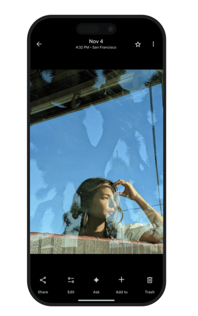 A woman is seen through a window with reflections of trees on the glass while looking outside, shown inside a smartphone interface.