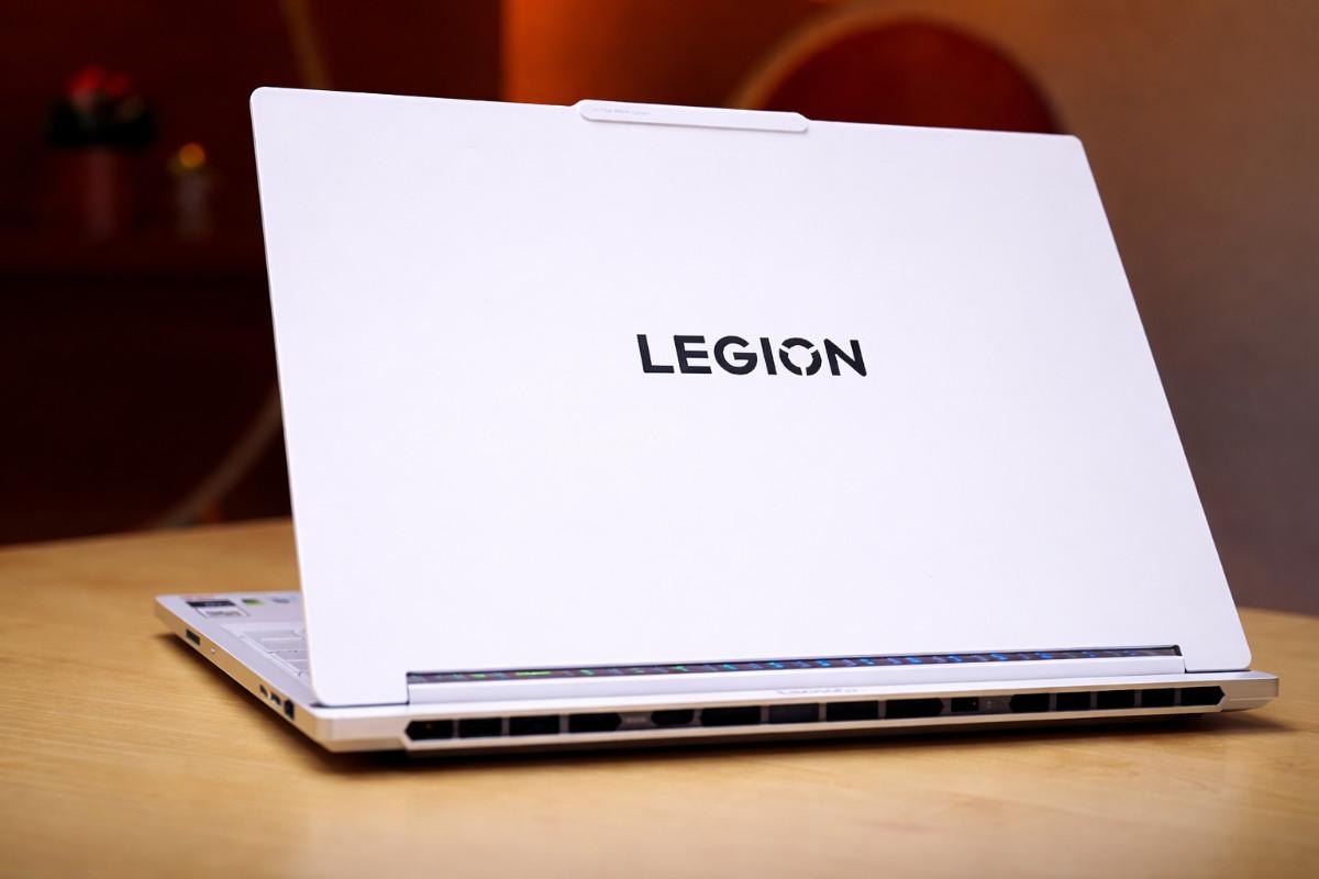 White Lenovo Legion gaming laptop open on a wooden desk, showing its rear vents and hinge design with the “LEGION” logo on the lid.
