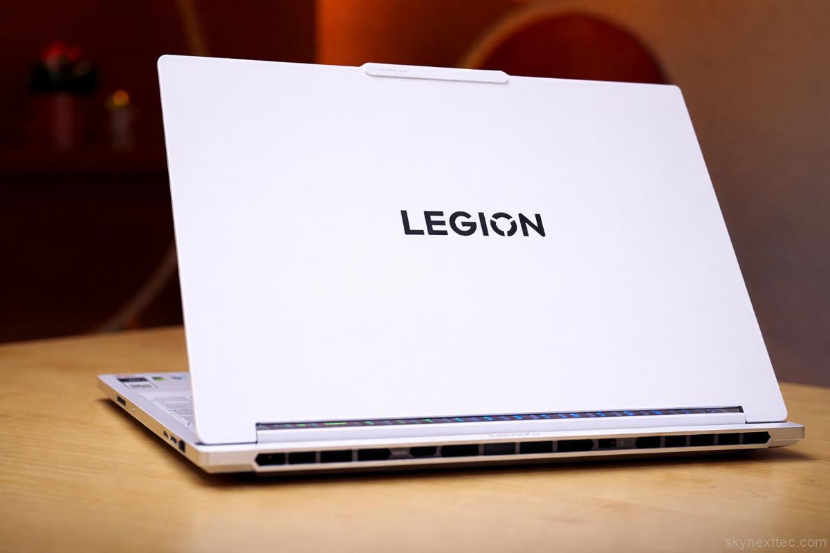 White Lenovo Legion gaming laptop open on a wooden desk, showing its rear vents and hinge design with the “LEGION” logo on the lid.